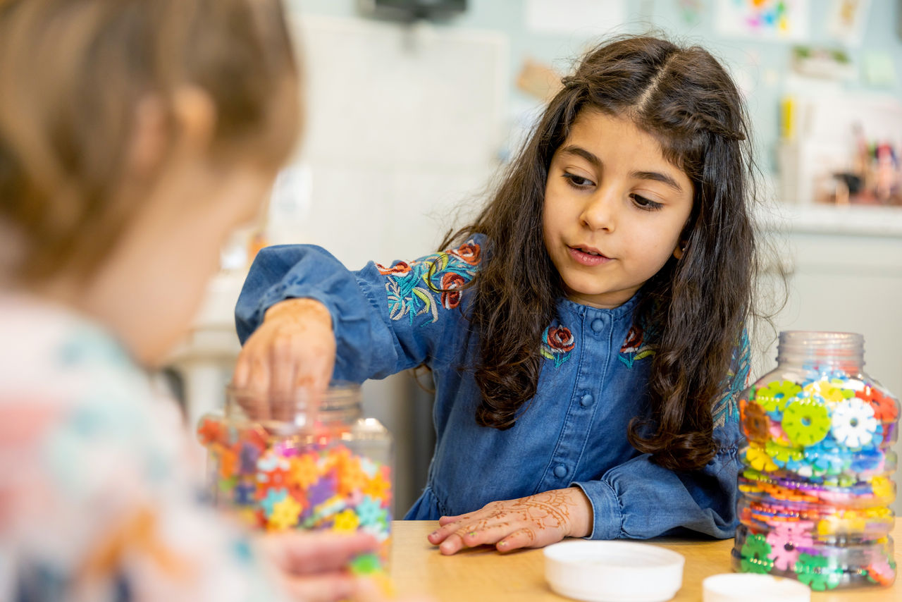 A child sitting at a table with craft supplies in a kindergarten classroom