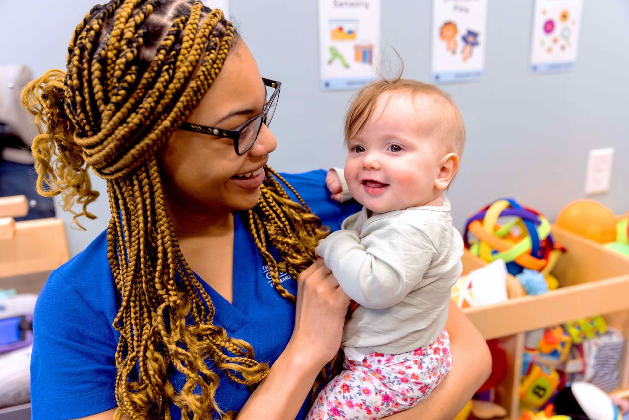 A smiling teacher holding a smiling infant 