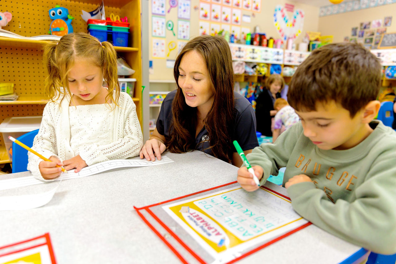 A teacher watching children complete handwriting worksheets