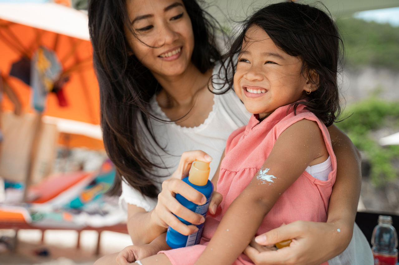 Mother applying spray sunscreen on her child